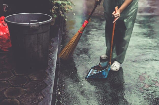 A person wearing gloves and using a specialized brush to clean the inside of a large rain barrel, demonstrating responsible maintenance practices for a home rainwater harvesting system.