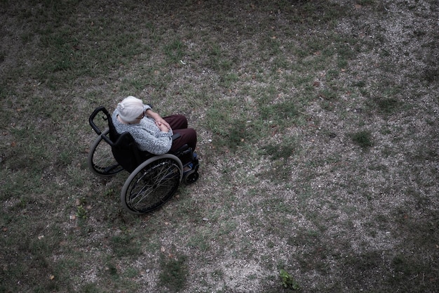 An elderly person in a wheelchair, looking frail, with a blurred industrial background and hazy sky, symbolizing the vulnerability of the elderly and marginalized communities.