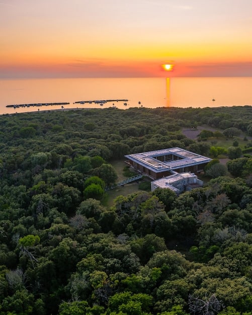 A modern, eco-friendly resort building amidst lush coastal dunes, featuring solar panels on its roof and large windows allowing natural light, demonstrating sustainable architectural design in a coastal setting.