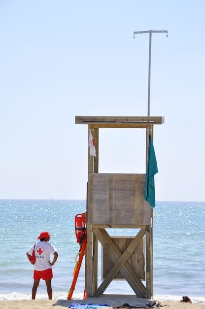 A lifeguard sitting on a high stand, scanning the beach and water for any signs of distress. The red and yellow flag is visible.