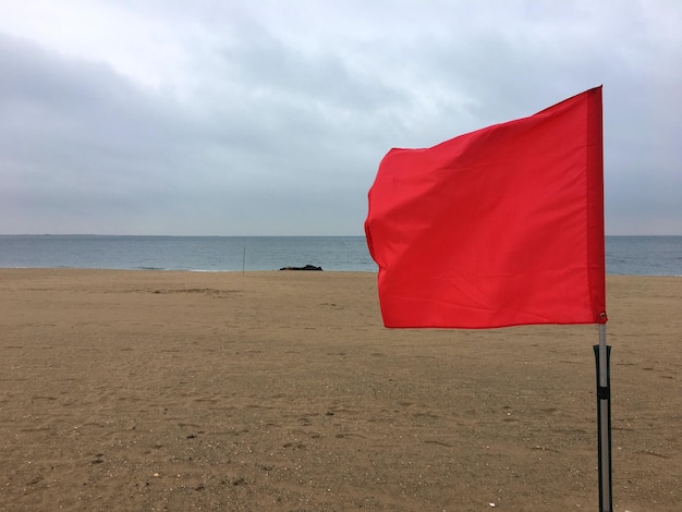 A detailed close-up of a red beach warning flag waving against a clear blue sky.